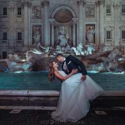www.fotokutkowska.pl - Para młoda w tańcu przed oświetloną Fontanną di Trevi w Rzymie, panna młoda w białej sukni z koronkową górą, pan młody w czarnym smokingu z muszką.