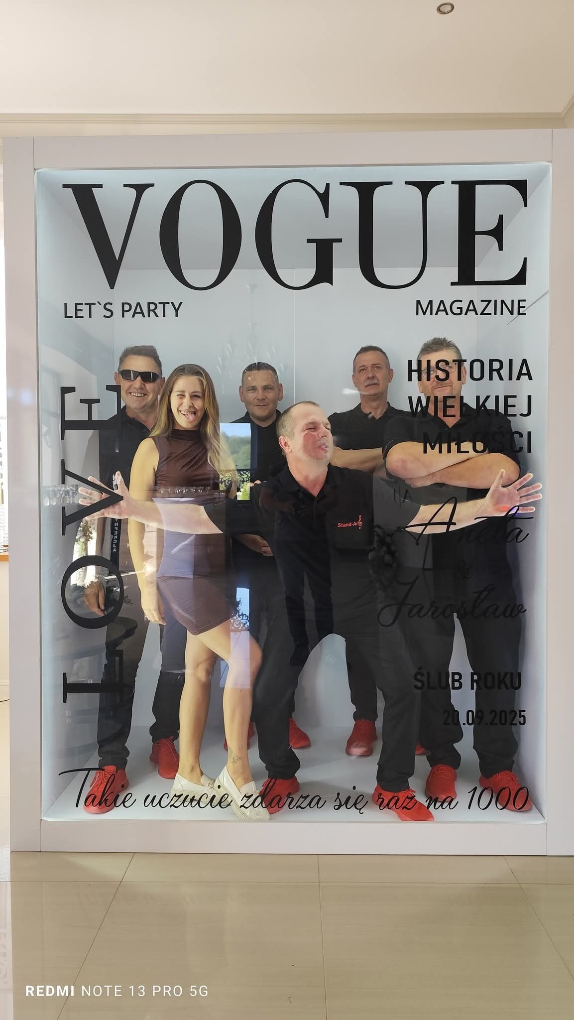 Zespół muzyczny pozuje za szybą z napisem 'Vogue', 'Let's Party', 'Historia Wielkiej Miłości', 'Ślub Roku 20.09.2025'. Uczestnicy w czarnych strojach i czerwonych butach.