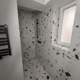 Wykończona łazienka z kabiną prysznicową wyłożona płytkami w stylu lastryko, z czarną armaturą i grzejnikiem drabinkowym.