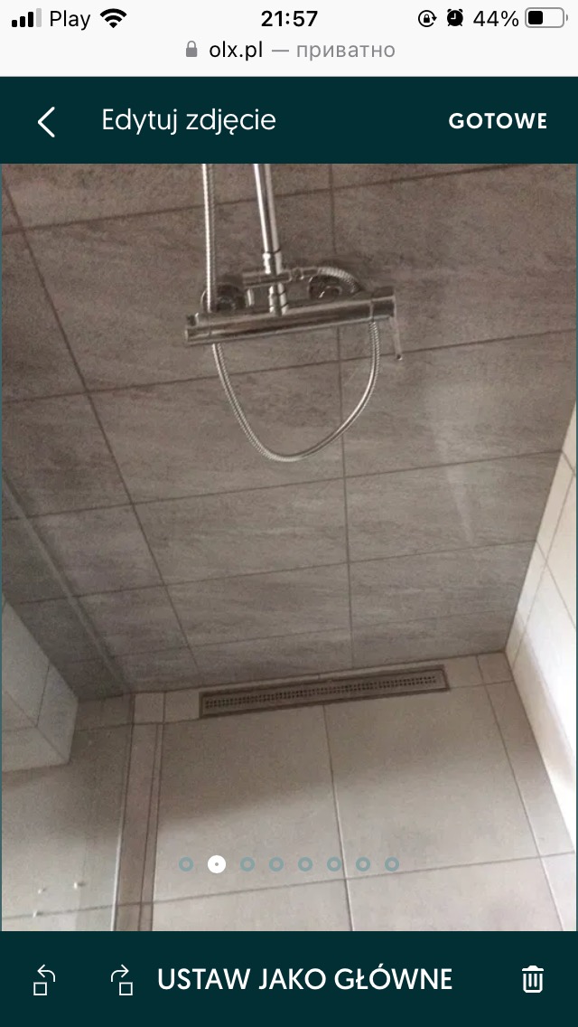 Szare płytki ceramiczne na ścianach i suficie kabiny prysznicowej z odpływem liniowym i chromowaną deszczownicą.