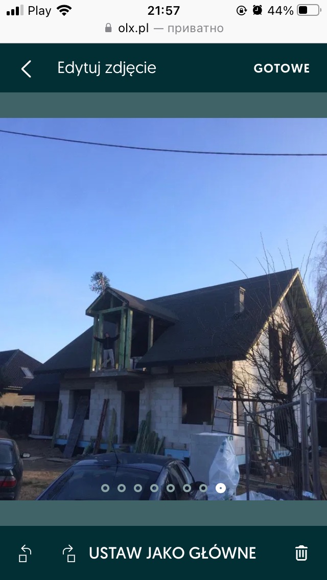 Dom w stanie surowym zamkniętym z widoczną konstrukcją dachu i oknami, z osobą stojącą w otworze okiennym na poddaszu, widok z zewnątrz w słoneczny dzień.