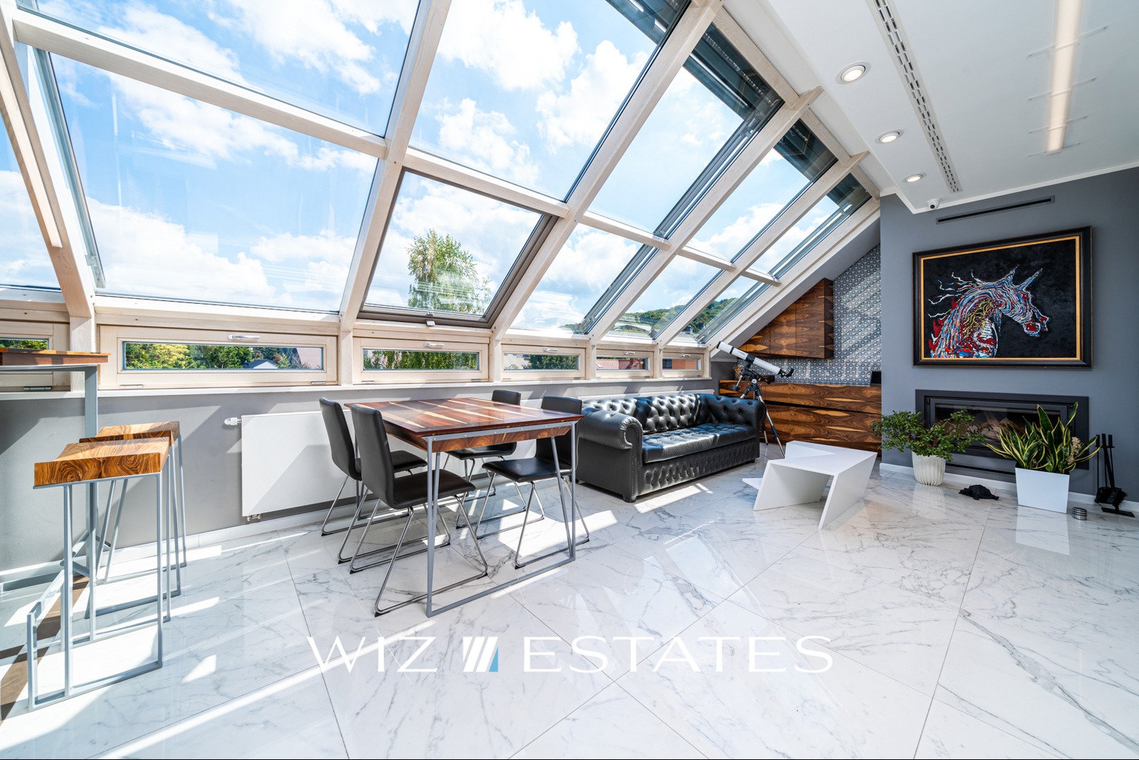 Jasne poddasze z dużymi oknami dachowymi, marmurową podłogą, skórzaną sofą Chesterfield, teleskopem i nowoczesnym obrazem z jednorożcem nad kominkiem.