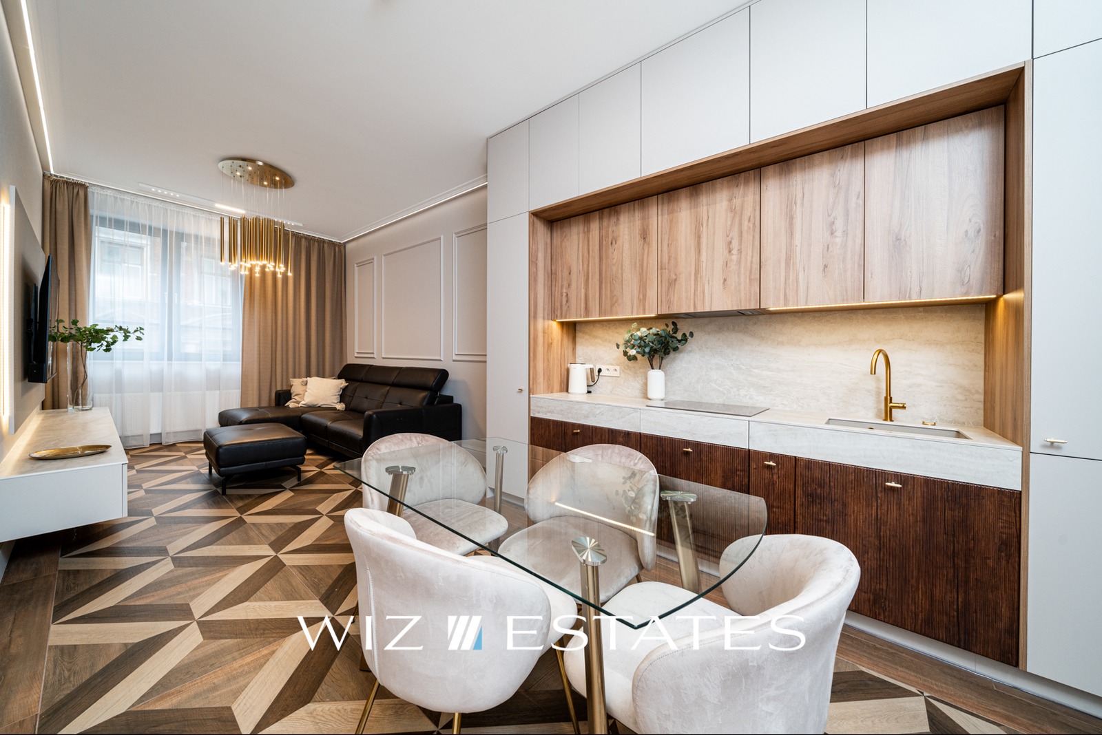 Nowoczesne wnętrze mieszkania: parkiet w geometryczny wzór, skórzana sofa, przeszklony stół z welurowymi krzesłami i zabudowa kuchenna z drewnianymi frontami.