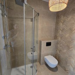 REMONTEX - wykończenia wnętrz RAFAŁ MARCZUK - Nowoczesna łazienka z kabiną prysznicową typu walk-in, podwieszaną toaletą i dekoracyjną ścianą w jodełkę, oświetlona lampą z wikliny.