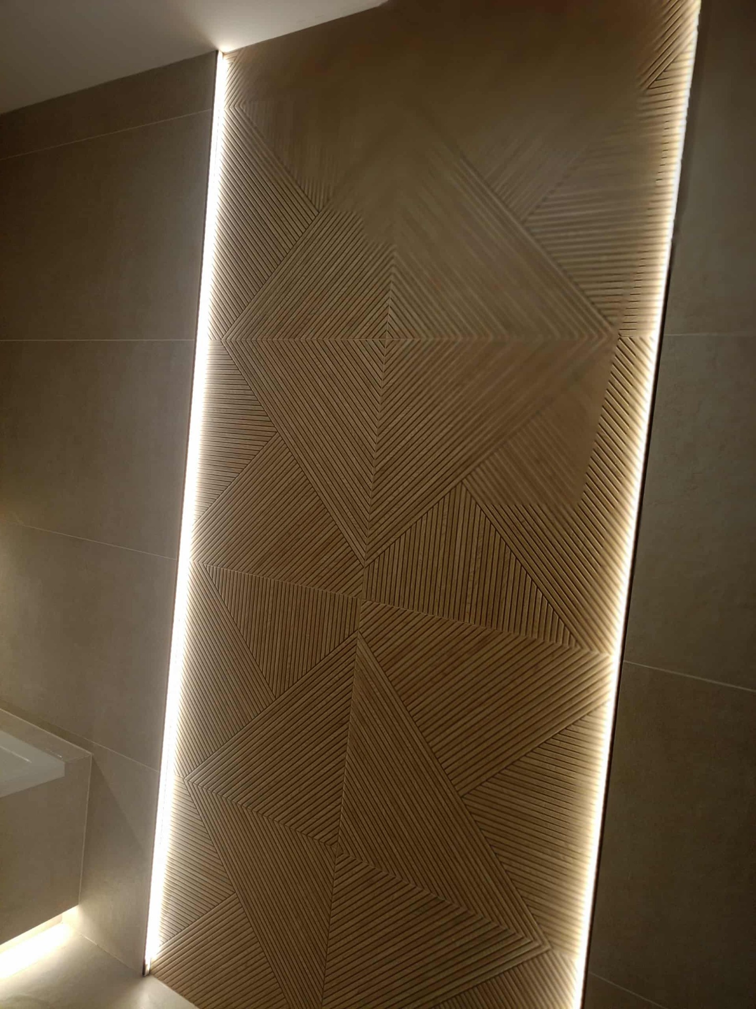 Dekoracyjna ściana z podświetleniem LED w łazience. Geometryczny wzór z drewnianych listewek tworzy unikalny efekt wizualny. Minimalistyczny design.