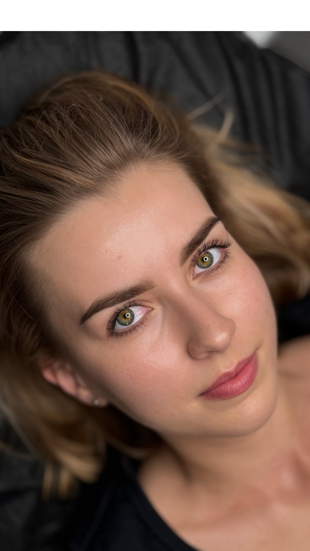 Portret młodej kobiety z delikatnym, naturalnym podkreśleniem brwi i rzęs, wykonany w zbliżeniu z góry.