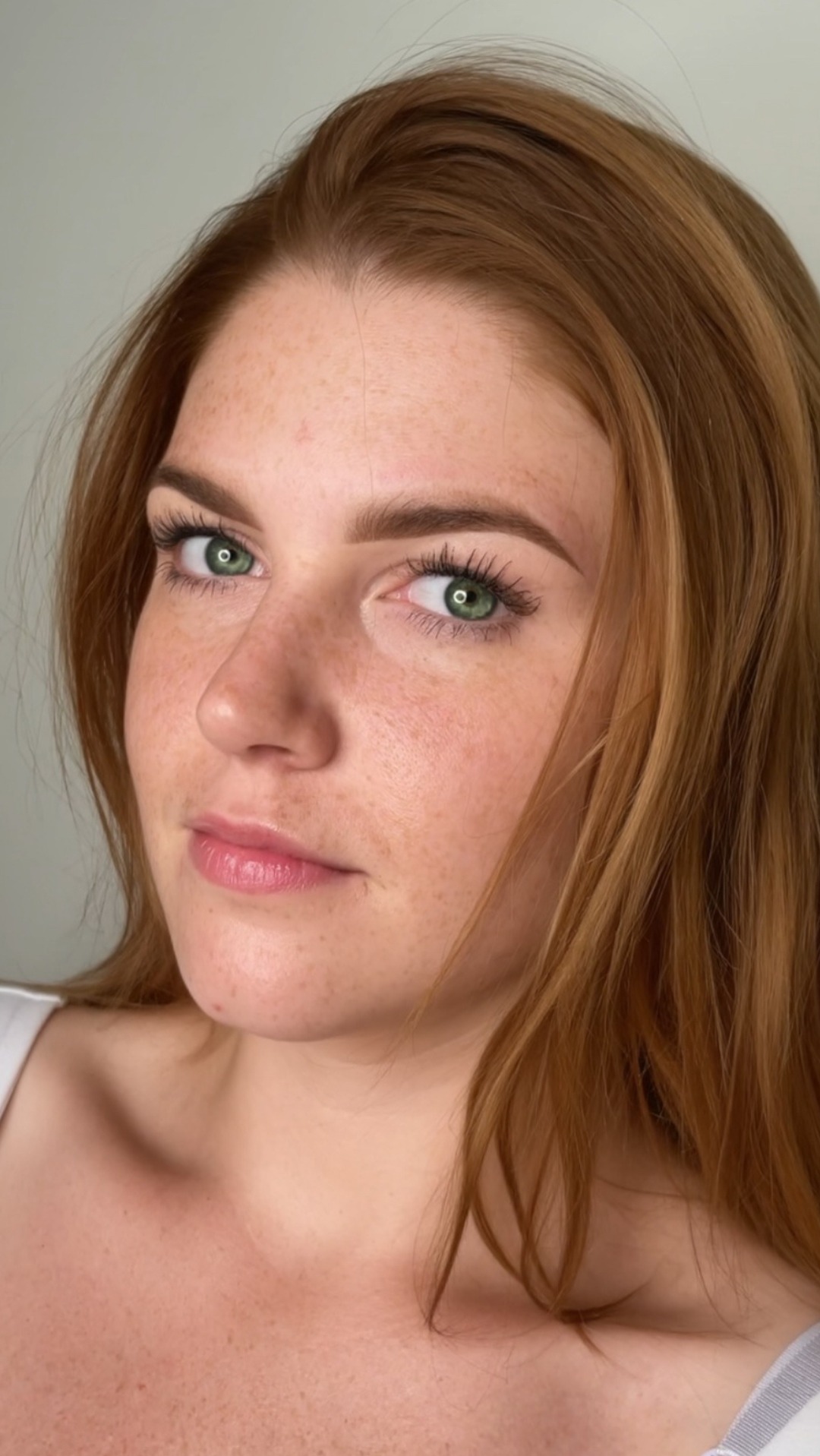 Portret kobiety z rudymi włosami, zielonymi oczami i piegami, z delikatnym podkreśleniem brwi i rzęs.