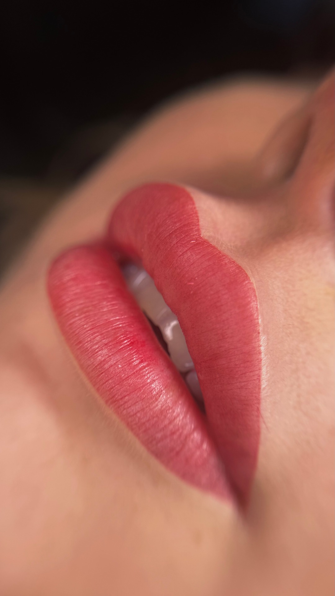 Zbliżenie na usta z trwałym konturem, lekko otwarte, widoczne zęby, delikatny błysk na ustach.