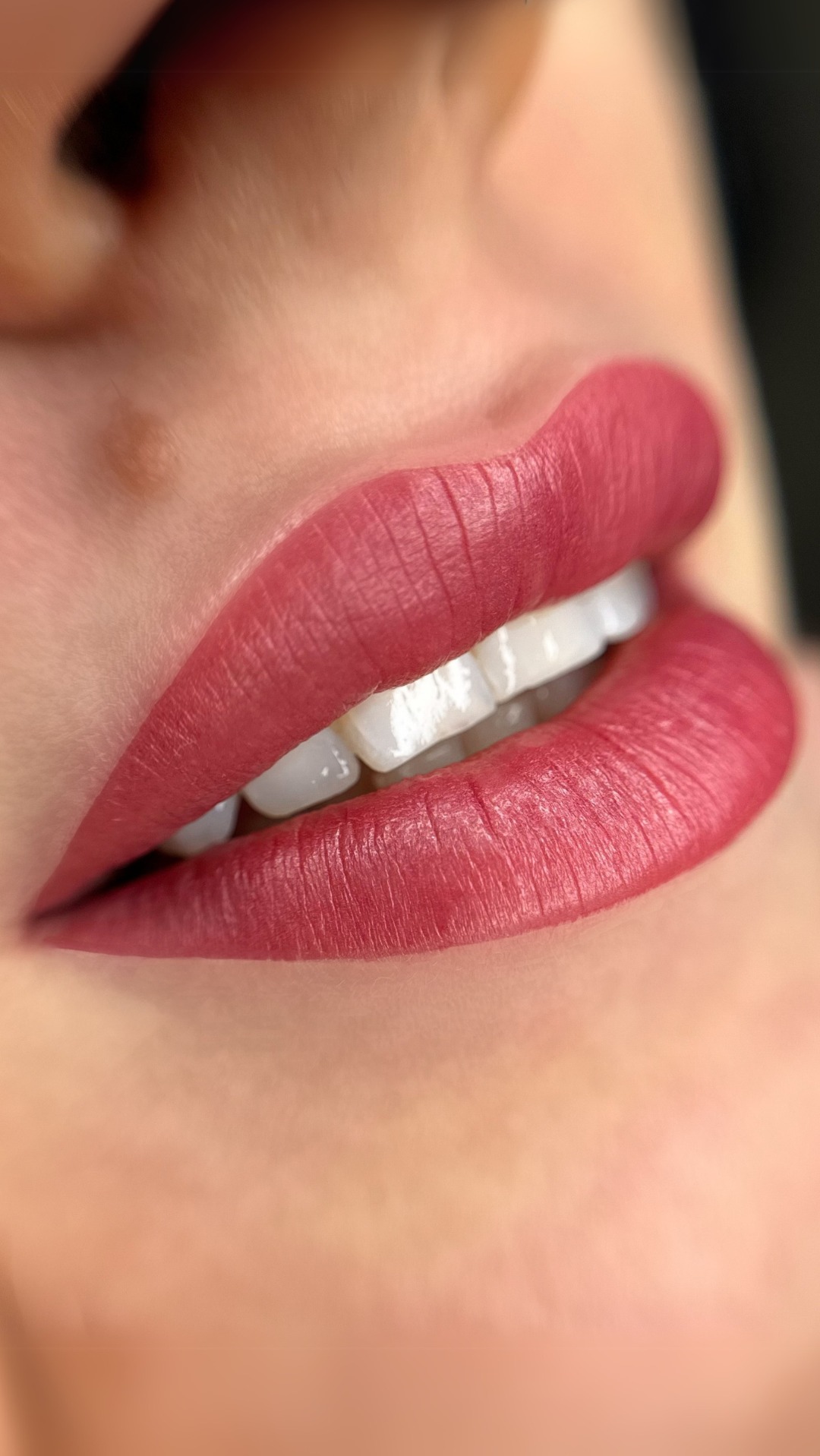 Zbliżenie na usta po zabiegu pigmentacji, widoczne idealnie podkreślone kontury i nasycony, matowy kolor w odcieniu malinowej czerwieni, z delikatnym połyskiem na zębach.