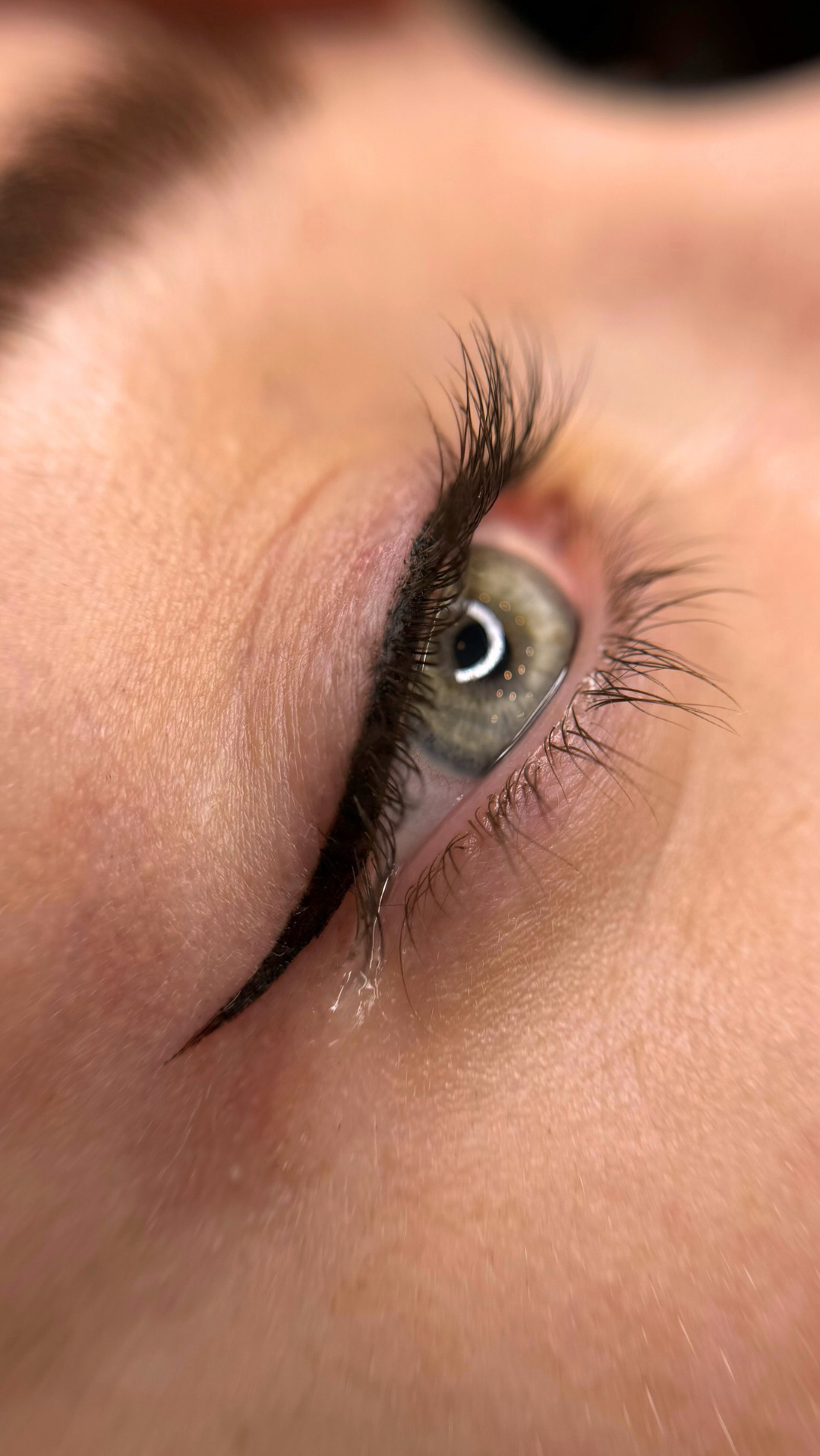 Zbliżenie oka z precyzyjnie wykonaną czarną kreską eyelinerem, podkreślającą linię rzęs; widoczne pojedyncze rzęsy i delikatna skóra powiek.