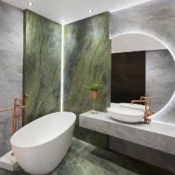 Elegancka łazienka z zielonymi marmurowymi ścianami, wolnostojąca biała wanna, umywalka nablatowa i okrągłe podświetlane lustro, akcenty w kolorze miedzi.