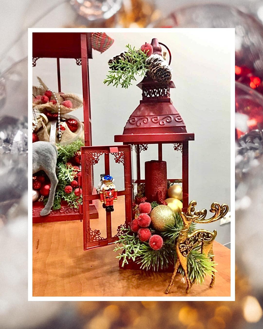 Czerwony lampion świąteczny z dekoracjami: figurka dziadka do orzechów, złoty renifer, bombki i gałązki świerku z czerwonymi owocami, tworzące bożonarodzeniową kompozycję.