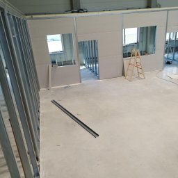 Artur Sarnecki - Wnętrze w trakcie budowy ścian działowych z profili metalowych i płyt gipsowo-kartonowych, widoczna drabina i elementy konstrukcyjne.