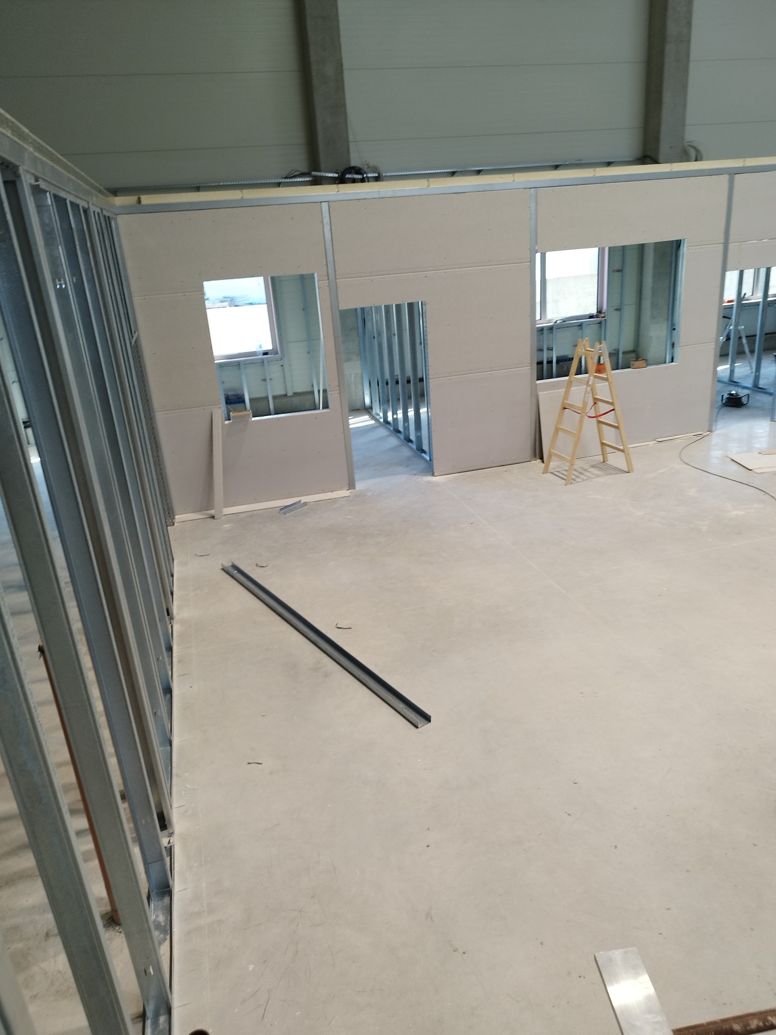 Wnętrze w trakcie budowy ścian działowych z profili metalowych i płyt gipsowo-kartonowych, widoczna drabina i elementy konstrukcyjne.