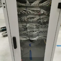 Szafa rack z zainstalowanymi przełącznikami sieciowymi i uporządkowanymi kablami ethernetowymi, widoczne oznaczenia portów i adresacja.