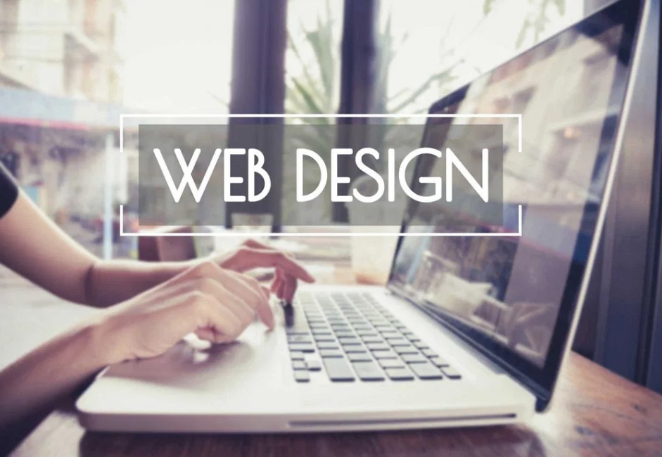 Osoba pisząca na laptopie z wyświetlanym napisem 'Web Design' w prostokątnej ramce, widoczne odbicie otoczenia w ekranie.