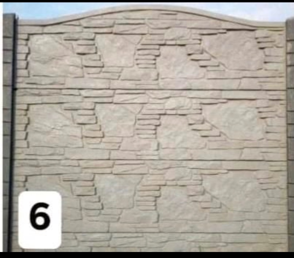 Fragment ogrodzenia z prefabrykatów betonowych imitujących kamień o nieregularnym kształcie, z widocznymi słupkami bocznymi.