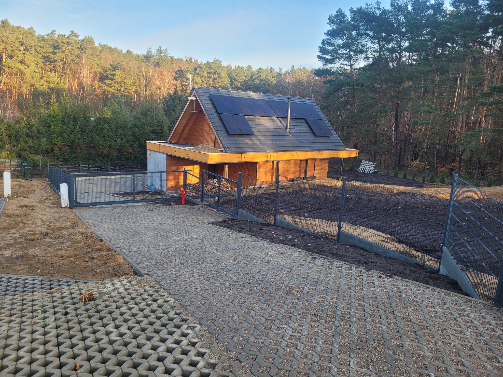 Nowoczesny dom z panelami słonecznymi widziany zza metalowego ogrodzenia w Chrzypsko Wielkie, widoczny fragment podjazdu z ażurowych płyt.