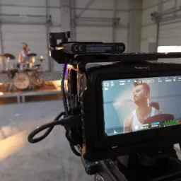 Ekran kamery Blackmagic Design podczas nagrywania perkusisty na scenie w hali, widoczny dysk 1TB podpięty do kamery.