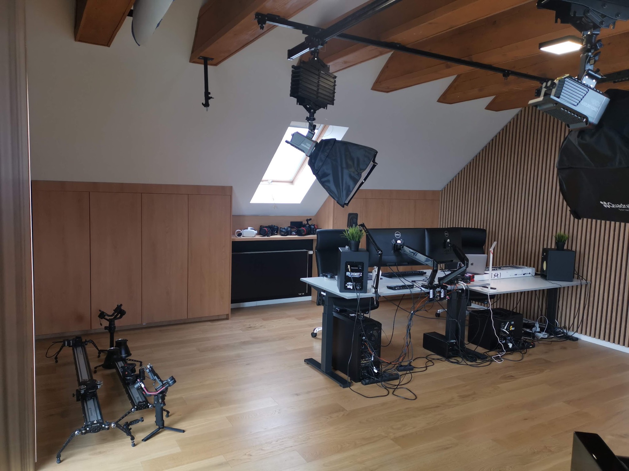 Studio filmowe w zaadaptowanym poddaszu z profesjonalnym oświetleniem, kamerami na szynach i stanowiskiem do montażu wideo z trzema monitorami.