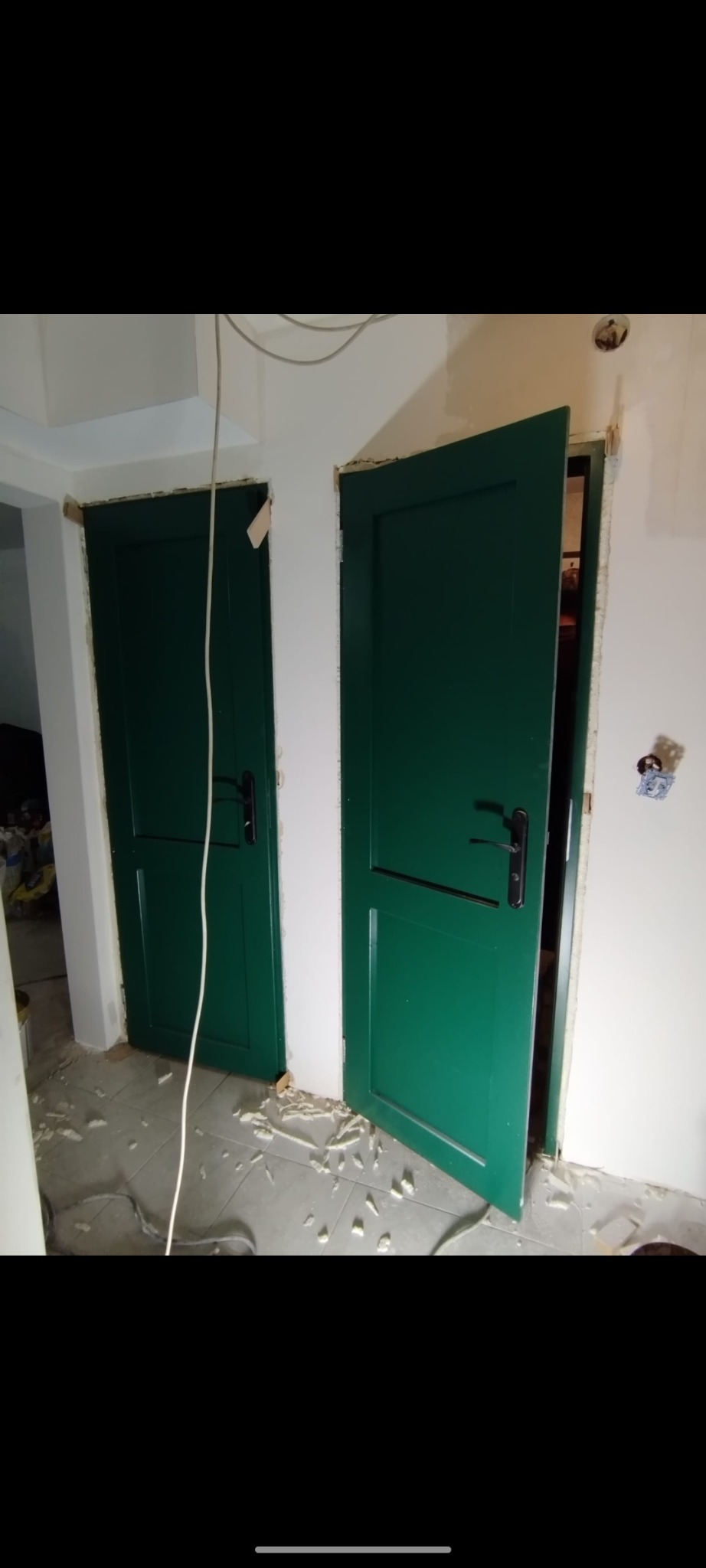 Montaż dwóch zielonych drzwi wewnętrznych z czarnymi klamkami; widoczne resztki pianki montażowej na podłodze i niedokończone wykończenie ścian.