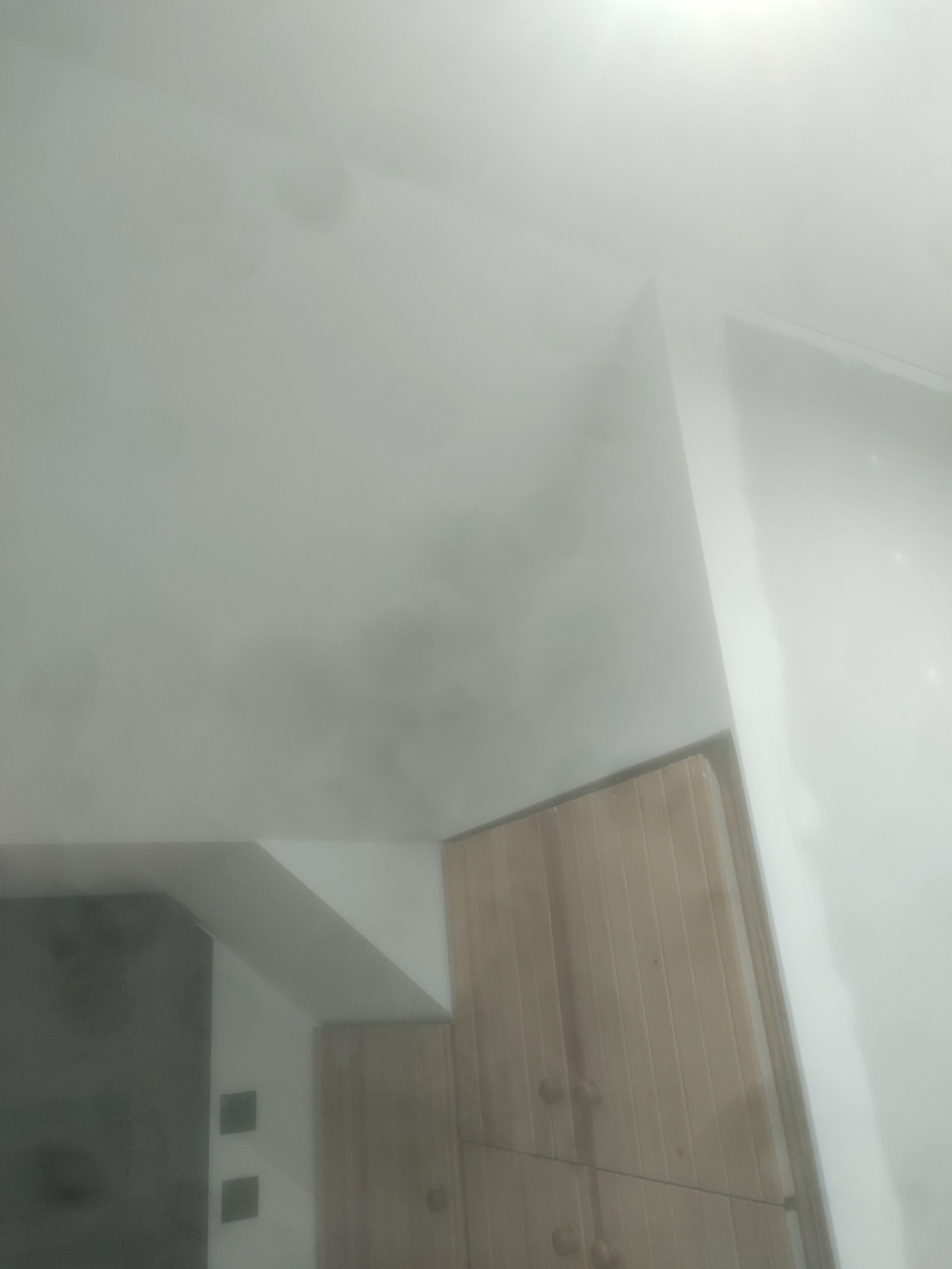 Niedokładne, amatorskie ujęcie sufitu z widocznymi plamami i fragmentem drewnianej szafki w rogu, słabe oświetlenie.