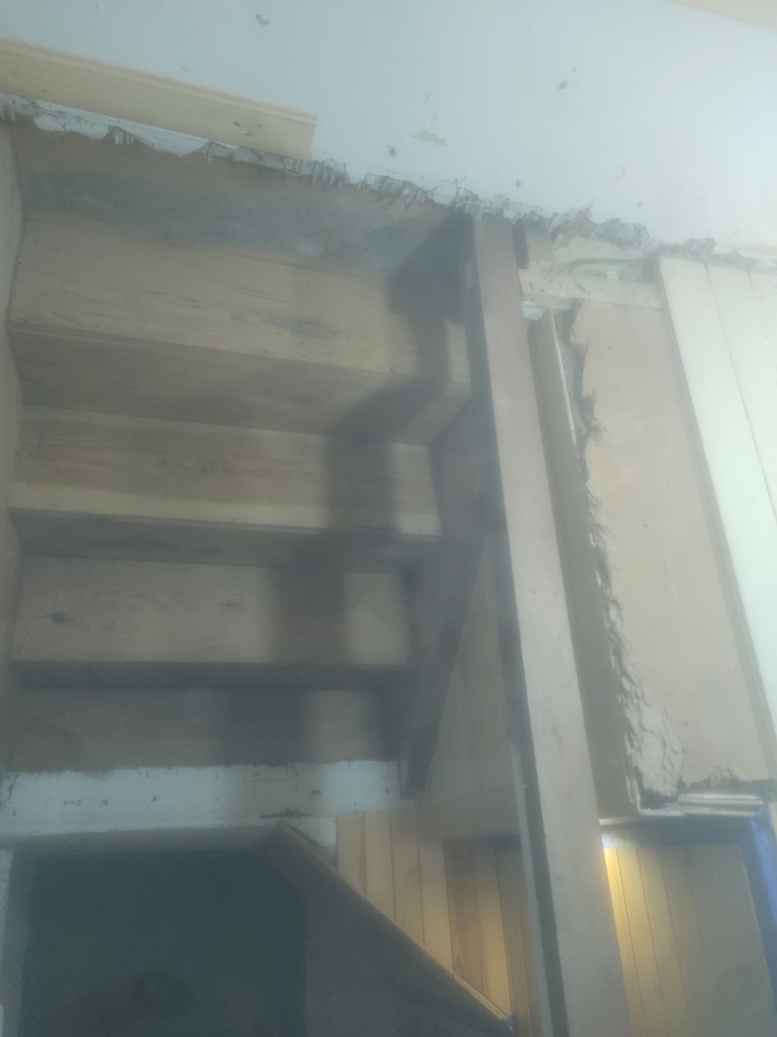 Drewniane schody w trakcie budowy, widoczne niedociągnięcia w wykończeniu ściany i sufitu, pionowy element konstrukcyjny z surowego drewna.