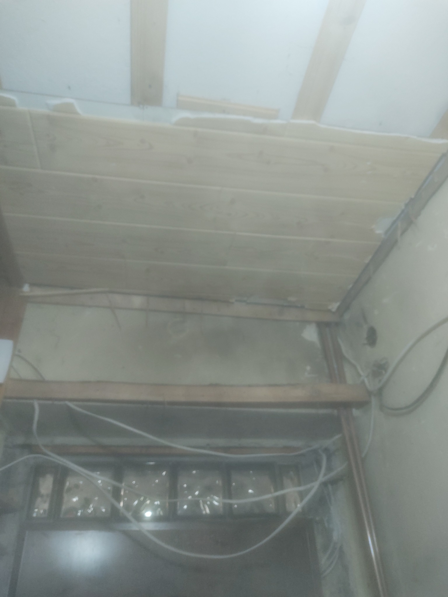 Montaż drewnianej podbitki sufitowej z widoczną izolacją, fragment ściany z przewodami i pustakami szklanymi w dolnej części kadru.