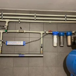 Instalacja uzdatniania wody z filtrami i zbiornikiem hydroforowym w Bochni, widoczne rury, zawory i lampa UV do sterylizacji wody.