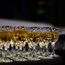 SEBASTIAN LAU VIRTUAL PARTNER - Rząd kieliszków wypełnionych złotym trunkiem, ustawionych na ciemnym tle, z widocznymi refleksami światła na szkle.