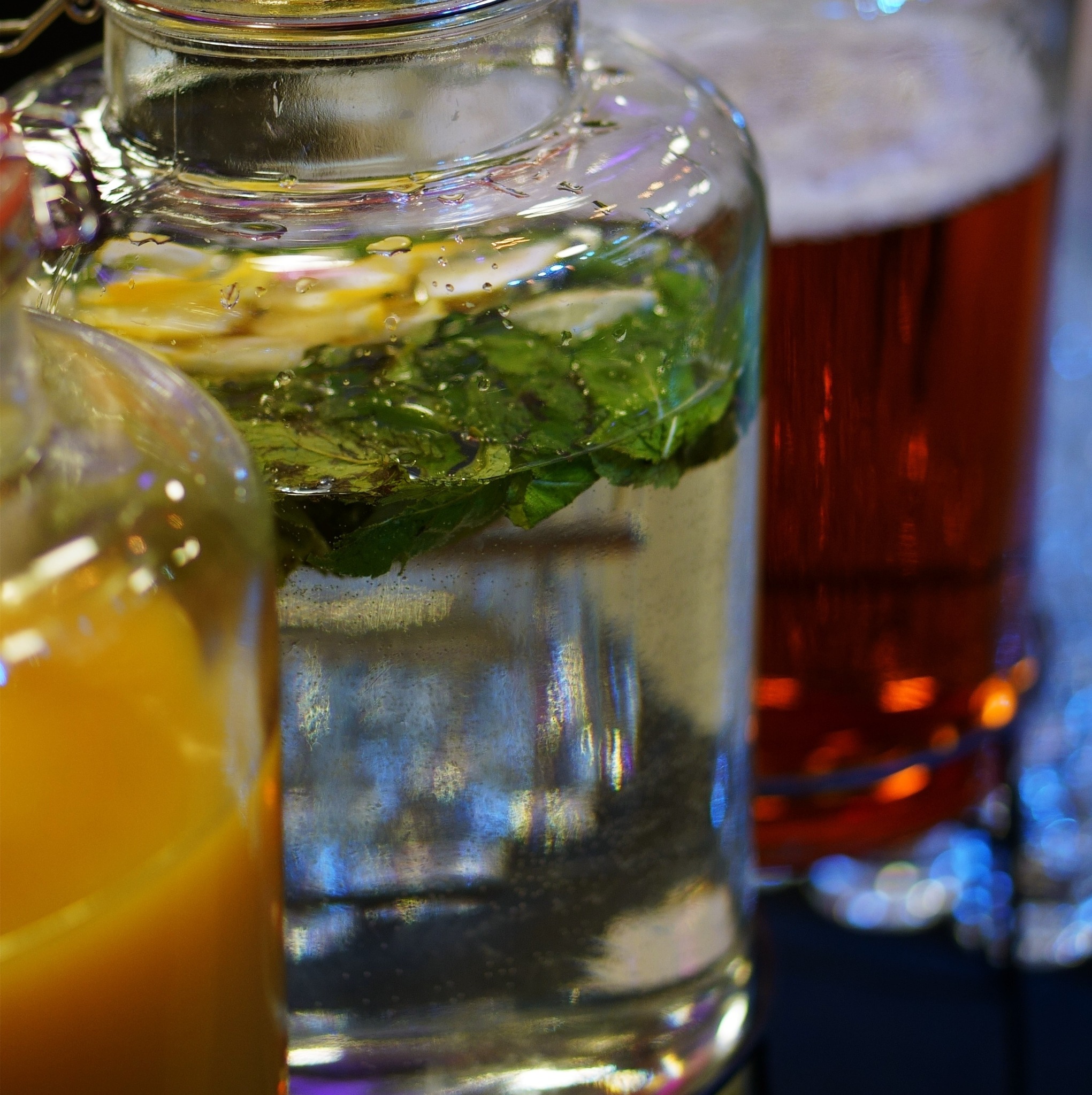 Zbliżenie na szklane karafki z napojami: pomarańczowy sok, woda z cytryną i miętą, oraz ciemny napój, prawdopodobnie piwo, przygotowane we Wrocławiu.