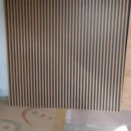 Panel ścienny z pionowych listew w kolorze drewna i grafitu, ustawiony na podłodze z wzorami, widoczne niedoskonałości podłoża.