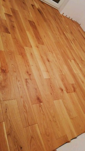 Nowo ułożona podłoga z jasnych, drewnianych desek, ułożonych w regularny wzór, widoczne listwy przypodłogowe w górnej części kadru.