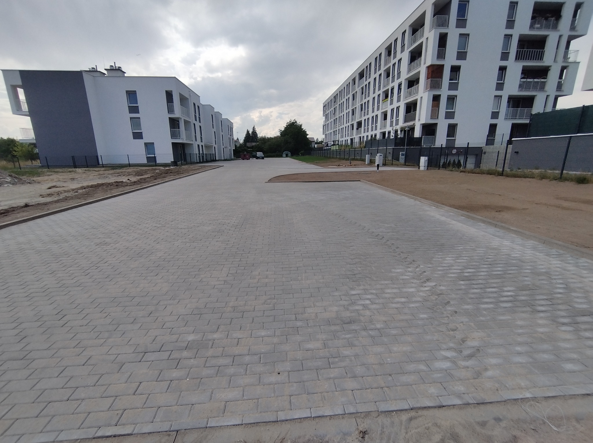 Nowo ułożona, szara kostka brukowa na szerokim podjeździe między nowoczesnymi budynkami mieszkalnymi w pochmurny dzień.