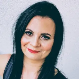 Portret uśmiechniętej brunetki z czerwonymi ustami na tle białej ściany.