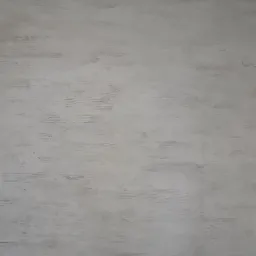 Szara, nier&oacute;wnomiernie nałożona warstwa tynku na ścianie wewnętrznej, widoczne ślady pędzla i niedoskonałości wykończenia, przy podłodze widoczna pomarańczowa cegła.