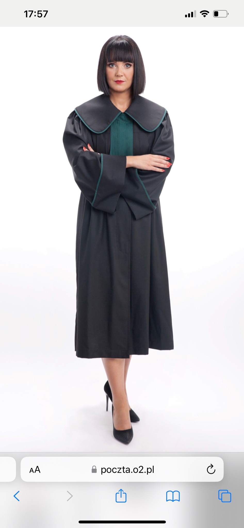 Portret kobiety w todze adwokackiej z zielonymi akcentami, na białym tle, z założonymi rękami i czarnymi szpilkami.