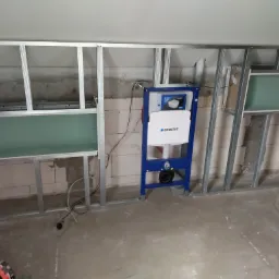 Stelaż podtynkowy Geberit zamontowany w metalowej konstrukcji z płyt karton gips w trakcie zabudowy w łazience, widoczne profile i płyty G-K.