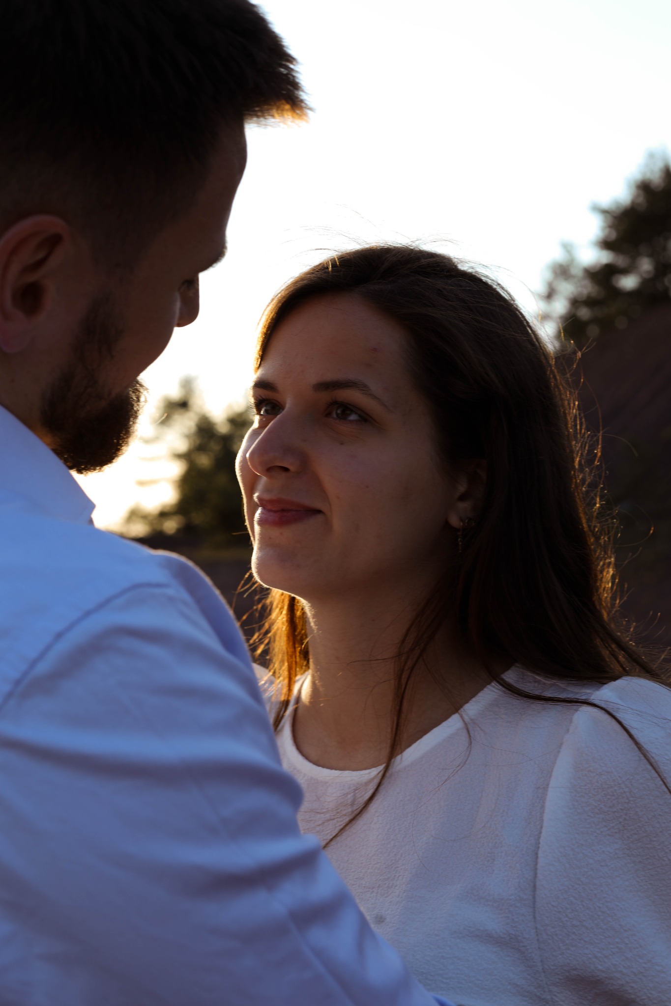 Zakochana para patrzy na siebie w ciepłym świetle zachodzącego słońca, kobieta w białej bluzce, mężczyzna w błękitnej koszuli.