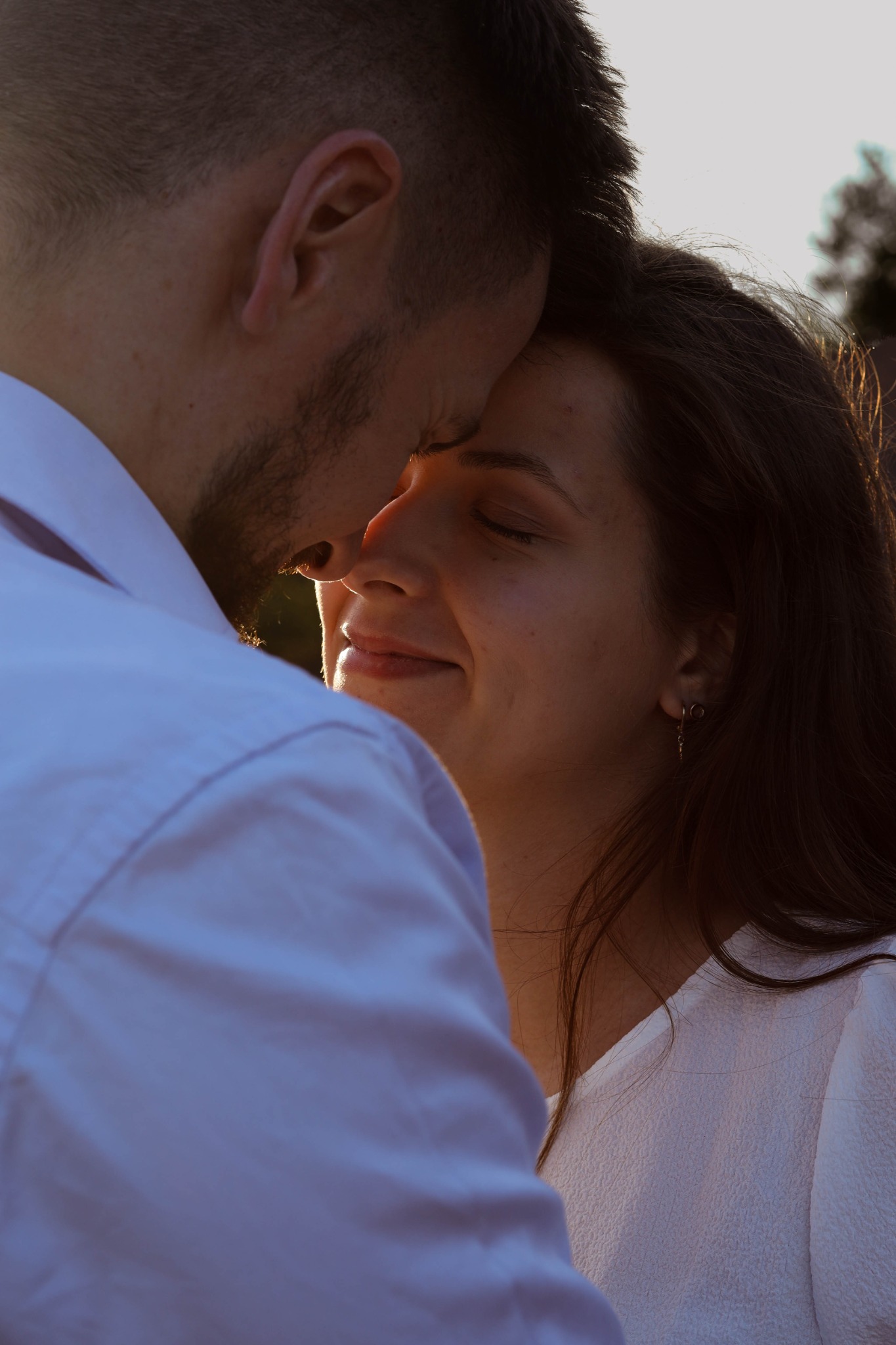 Zbliżenie na twarze pary: mężczyzna z brodą i kobieta z kolczykami, złączeni czołami w intymnym geście na tle rozmytej zieleni.