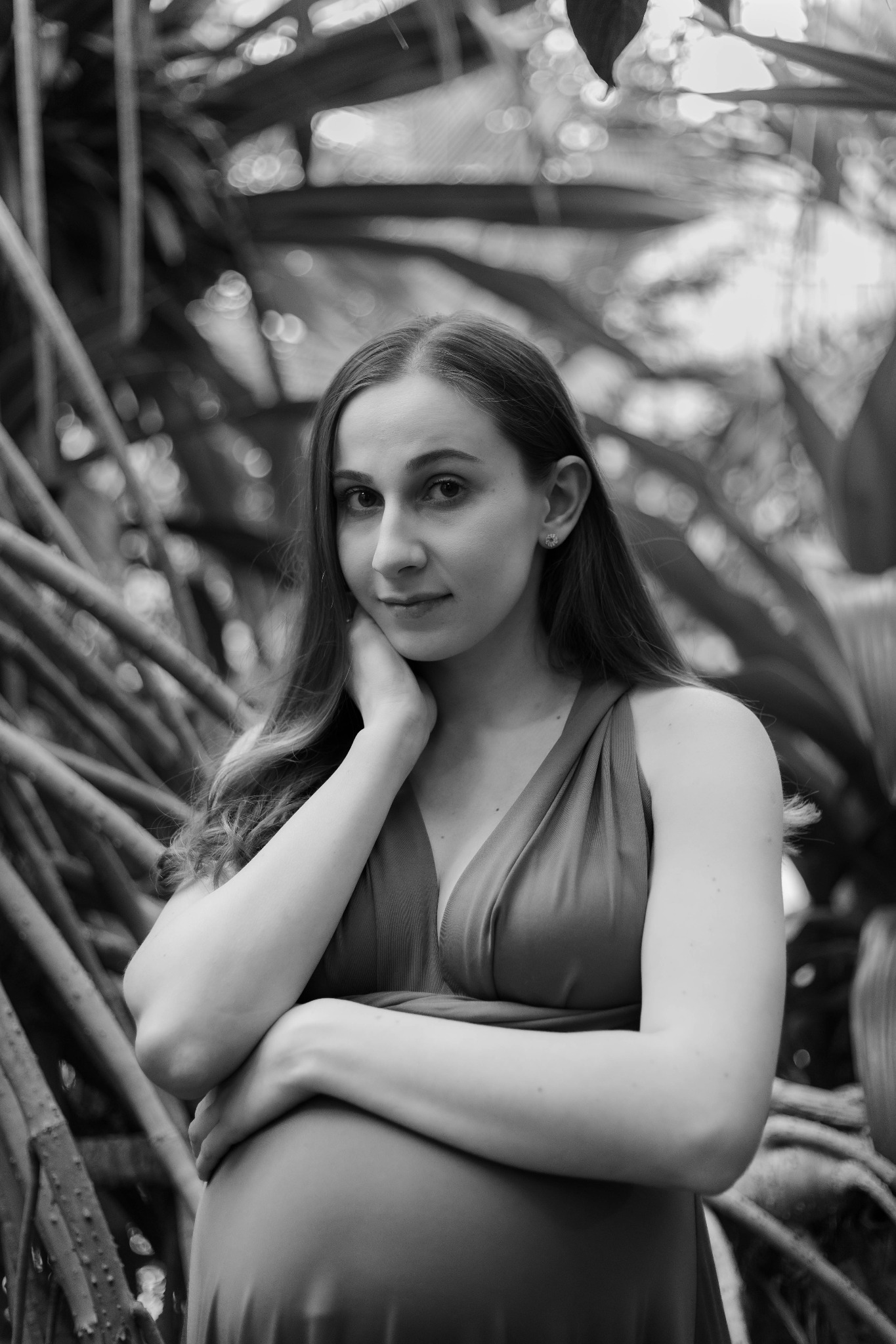 Portret kobiety w sukience, z ręką podpartą pod brodą, na tle egzotycznych roślin i pnączy w czerni i bieli.