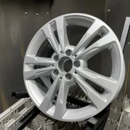 Aluminiowa felga samochodowa po procesie malowania proszkowego, zawieszona na metalowej konstrukcji w komorze lakierniczej.