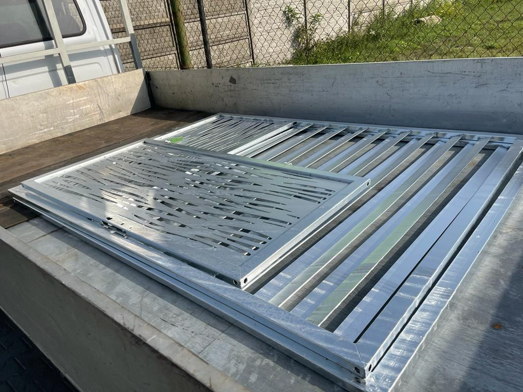 Elementy metalowe ogrodzenia, w tym panel z wycinanym wzorem, transportowane na pace samochodu dostawczego, gotowe do montażu.
