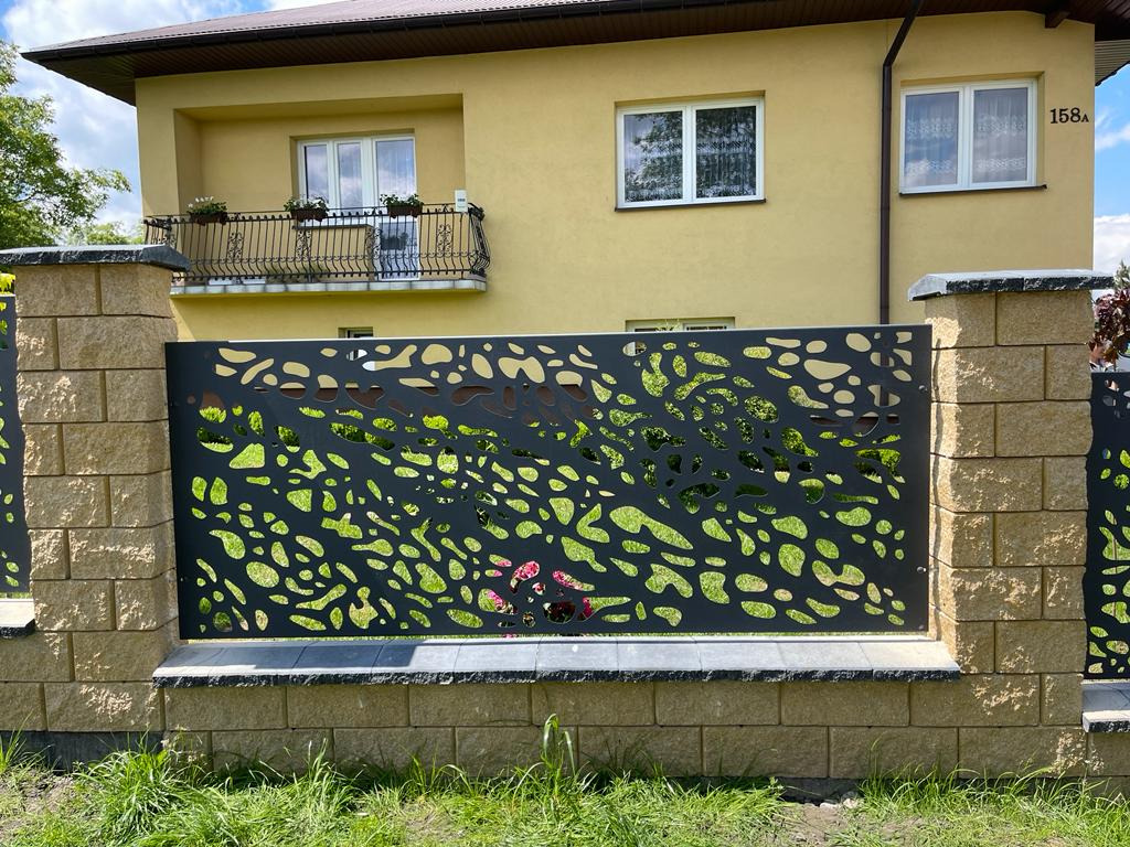 Nowoczesne ogrodzenie z ażurowym, abstrakcyjnym wzorem na tle żółtego domu z balkonem