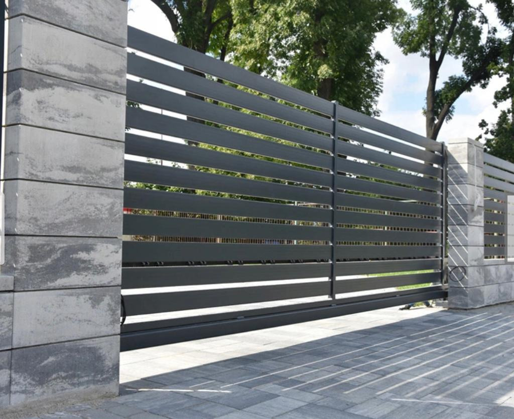 Nowoczesna, przesuwna brama wjazdowa z poziomych profili, osadzona na słupkach z szarej, warstwowej kostki betonowej, z widocznym fragmentem podjazdu z kostki brukowej.