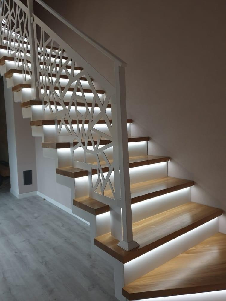 Nowoczesne schody drewniane z białymi podstopnicami i ażurową balustradą, podświetlone ledami od spodu, widok z dołu.