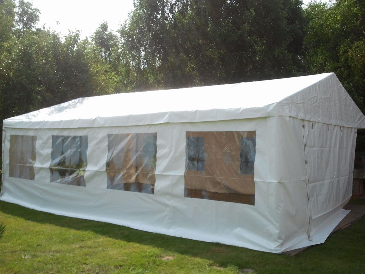 Biały namiot eventowy z przezroczystymi oknami ustawiony na trawie, widok z boku, drzewa w tle.