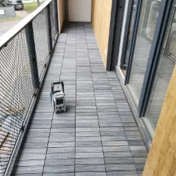 Szare panele podłogowe ułożone na balkonie z czarną metalową barierką, obok stoi przenośne radio budowlane marki Makita.