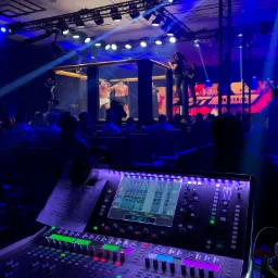 Panel mikserski z listą walk MMA w tle, oświetlenie sceniczne i publiczność podczas wydarzenia sportowego.