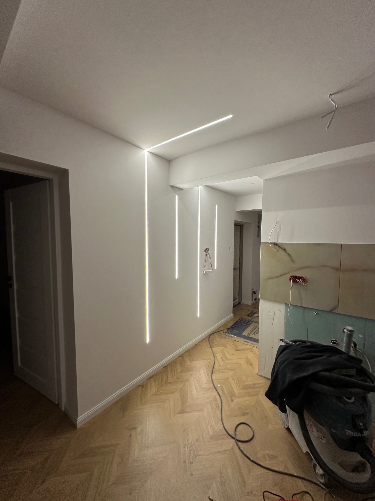Nowoczesne oświetlenie LED w remontowanym wnętrzu. Widoczne pionowe i poziome linie świetlne na ścianach, parkiet oraz fragmenty płytek i narzędzi.